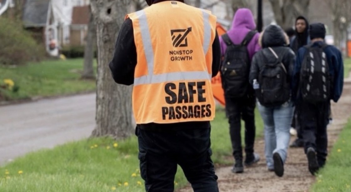 A Safe Passages team member in an orange vest walks with Akron students along a school route.