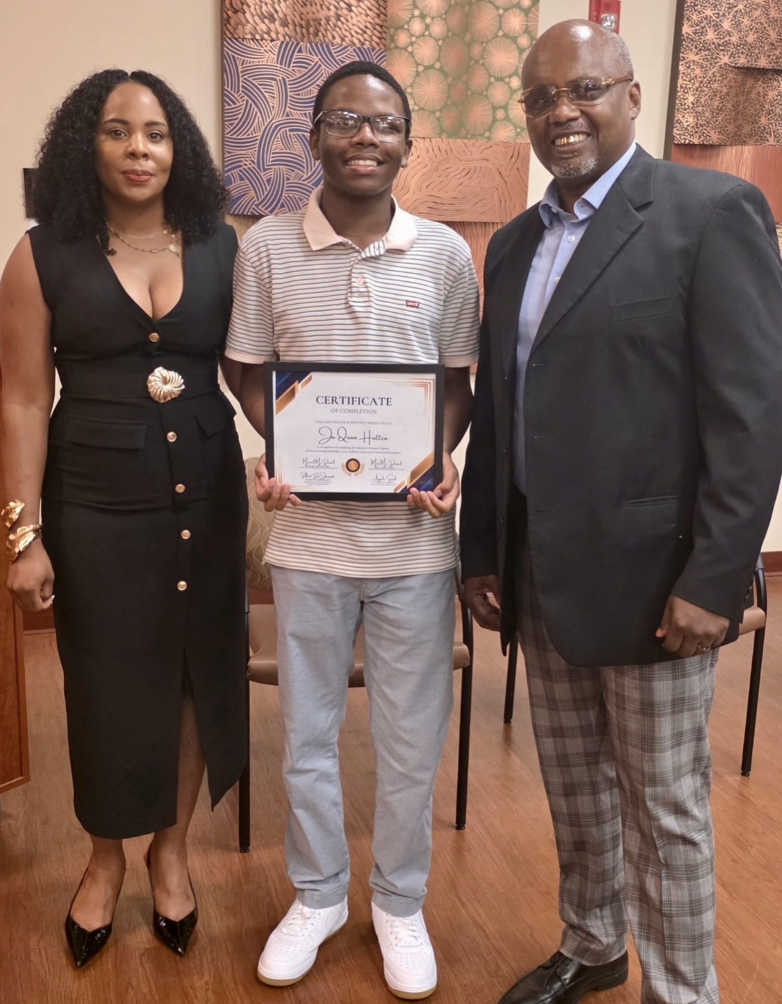 A Pathway to Purpose graduate holding a certificate of completion with Mia and Marcel McDaniel.